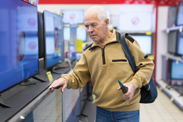 elderly man choosing TV in showroom of electronics store