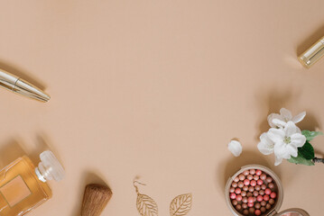 Frame with a set of makeup cosmetics, flowers and other accessories on a beige background. Composition in gold tones. Flat lay, top view.