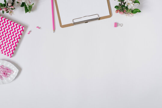 Home office desk workspace with blank paper clipboard, notepad, keyboard, stationery and apple tree flowers on white background with copy space
