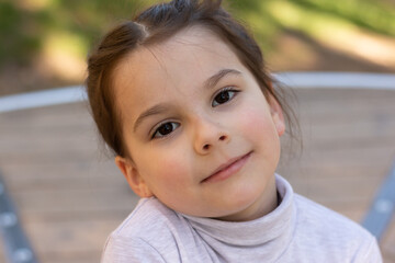 Close-up portrait of a little beautiful girl in a turtleneck sweater in the park