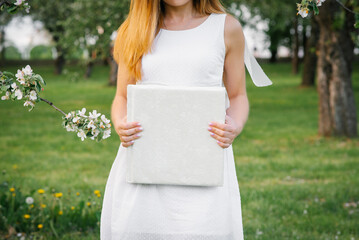 A white-covered wedding photo album is held by a woman in a white dress