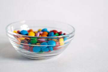 A lot of colorful round candies, taken in close-up, a vase with pills shifted to the left