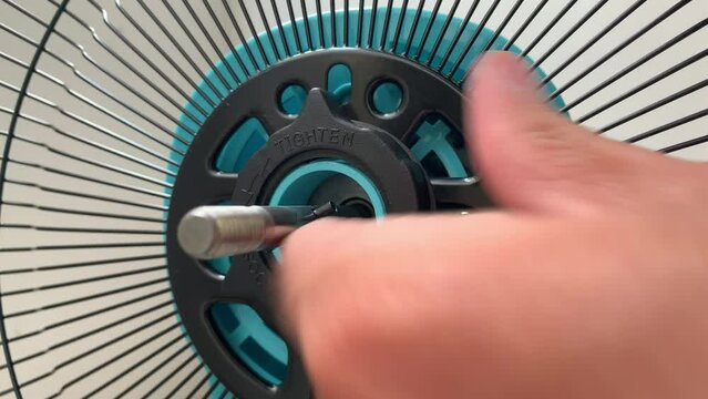 Loosen black plastic nut from rear grille bar on blue desk electric fan. Hand uninstalling rotate counterclockwise to unlock the black screen with the motor housing daytime. - DIY household concept 