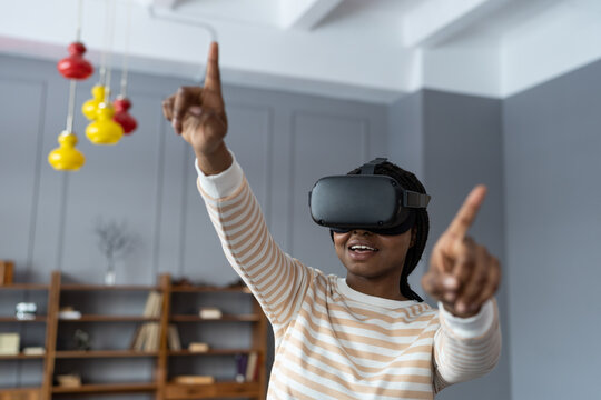 Smiling African American girl interacting with 3d visualization, first virtual reality experience in digital simulation app. Future trend using vr goggles device for video game and home entertainment