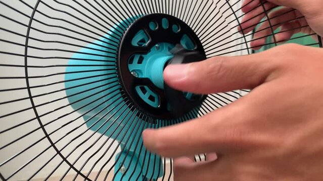 Loosen black plastic nut from rear grille bar on blue desk electric fan. Hand uninstalling rotate counterclockwise to unlock the black screen with the motor housing daytime. - DIY household concept 