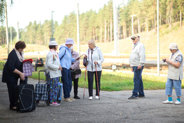 A group of elderly friends with suitcases and bags gather at the train station to go on a trip