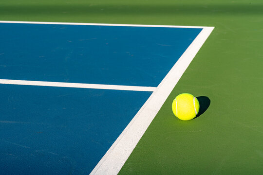 Yellow tennis ball at blue tennis court with white baseline and green out of bounds