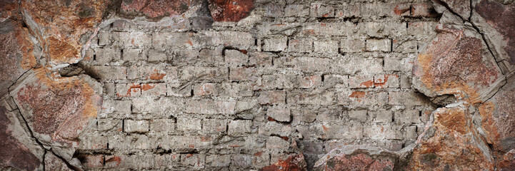 Old brick wall with chipping natural stone cladding. Vintage brickwork texture. Grunge background with space for design. Rough dirty distressed surface. Broken facade of the building. Wide banner.