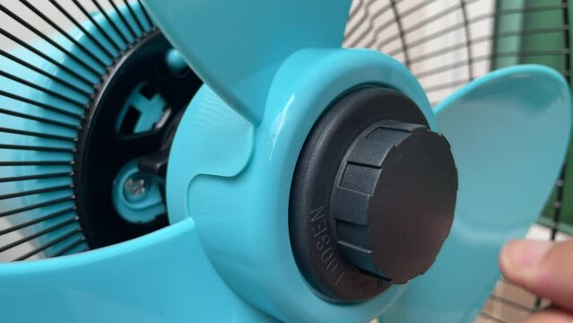 Loosen black plastic nut from blue blade electric fan. Hand unfasten bolt rotate spinning clockwise uninstall to unlock fan blade daytime. - DIY household self assembly concept