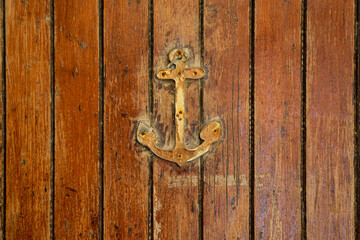 Close-up of a weathered wooden door decorated with a small rusty anchor