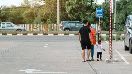 Back view of Asian family on the way back to car parking lot. Parents take care and hold their young son by hand as they walk back to the car at outdoor parking lot. Family care and concern concept.