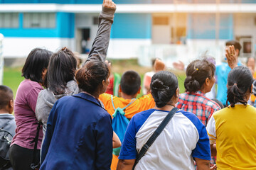 Obraz premium Back view of Moms watch and cheering their sons playing football in school tournament on sideline. Sport, outdoor active, Spectator watching soccer game. Parents care and encourage their children.