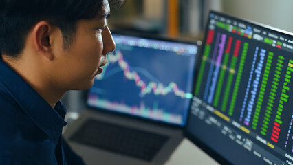 Young Asian investor man watching the change of stock market and trading stock on computer laptop screen.