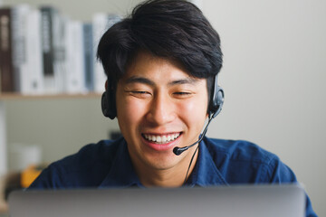 Young Asian man wearing headset talking on video call conference or virtual meeting at home via...