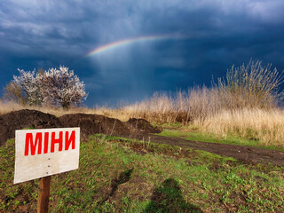 Mines sign on the field in Ukraine with dramatic sky and rainbow on the background.