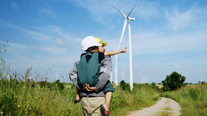 engineer father and his son playing Piggyback in a wind turbine field, father teaching his son how...