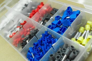 A set of colored crimp terminals for electrical wires. Crimping sleeves of different sizes. Plastic spare parts box for electrician. Toolbox. Selective focus
