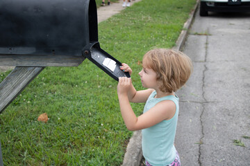 Young girl in teal tanktop checks postal mailbox while standing in the street