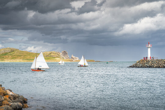 People on a small sailboats exiting Howth marina, passing Howth Lighthouse and per with Irelands Eye island in the background, Dublin, Ireland