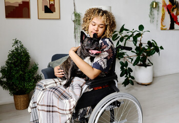 Fototapeta na wymiar African young girl with disability sitting in wheelchair with dog on her knees and enjoying their communication