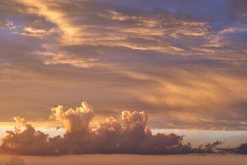 Bright colorful sunset sky with vivid smooth clouds illuminated with setting sun light spreading to horizon