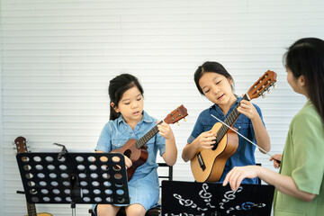 In a music school, a beautiful Asian teacher is teaching students to play music and sing, the concept of education, child development.