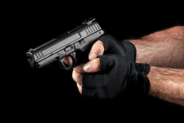 Closeup man hand with gloves holding gun with two hands and aiming down on black background. Finger on the trigger of the pistol. - obrazy, fototapety, plakaty