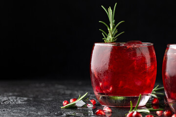 Pomegranate gin cocktail with lime, rosemary and ice on rustic black table