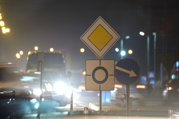 Roundabout road signs with blurred cars on city street traffic at night. Urban transportation...