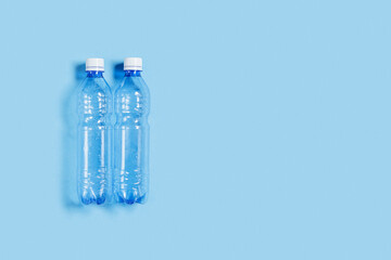 Two blue plastic bottles on blue paper background, top view empty plastic bottle for water, minimal style, copy space. Pollution, plastic garbage, environmental protection concept.