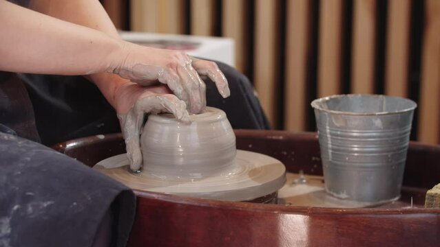 Hands of elderly woman making a hole in piece of wet clay and widing it on the pottery wheel