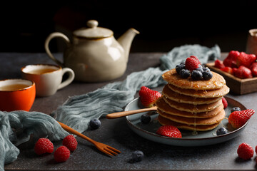 Pancakes sur une assiette couvert des fruits: framboise, myrtille. Le théière avec une tasse à...