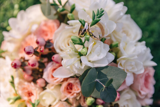 beautiful bridal bouquet of white and pink flowers with golden wedding rings on the grass.