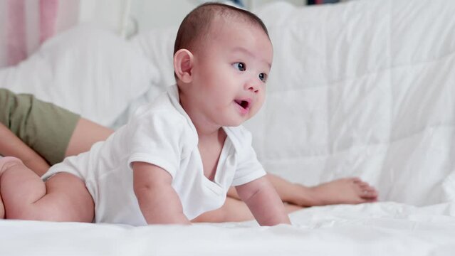 Cute Asian newborn baby boy lying play on white bed with smile happy face. While your mother takes care nearby. Little innocent new infant adorable child in first day of life. Mother's Day concept.