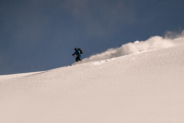 Great view on active snowboarder riding down from snowy mountain on splitboard and splashes snow.