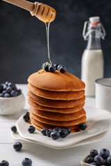 Pancakes sur une assiette couvert des fruits: framboise, myrtille. Miel qui coule sur les crêpes.