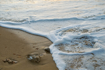 Welle am Strand mit Schaum bricht am Sandstrand auf Stein bei Sonnenuntergang Detail