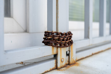 Rusty metal chain hanging on closed white window, close up.