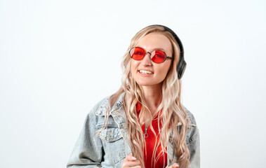 Blonde in headphones on a white background. She is wearing a denim jacket and red glasses.