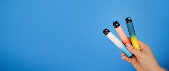 Disposable three electronic cigarettes in a woman's hand close-up on a blue background. The concept...
