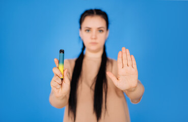 a girl on a blue background holds a disposable cigarette in one hand and shows a stop to smoking with the other hand. the concept of a healthy lifestyle