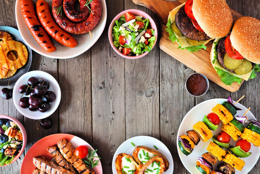 Summer BBQ or picnic food frame. Assorted burgers, grilled meat, vegetables, fruits, salad and potatoes. Above view on a dark wood background. Copy space.