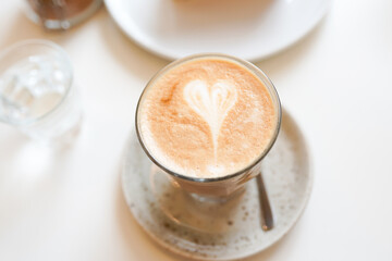 a cup of coffe latte with heart on white table in the cafe