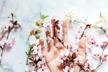 Female hand with pink almond flowers coming out of the sleeve on marble background. Spring concept. Horizontal.