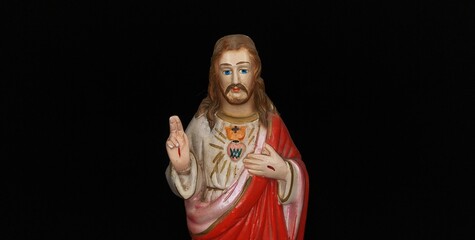 Old vintage wooden idol of Blessing Jesus Christ christian god Statue face holy bleeding hand wound and Sacred Heart isolated on black background and copy space. Beautiful close up macro side view. - obrazy, fototapety, plakaty