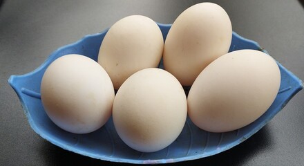 Heap of several isolated farm fresh organic white duck or hen raw eggs on isolated on a blue plate with black table background surface and copy space. Beautiful horizontal close up macro top view.
