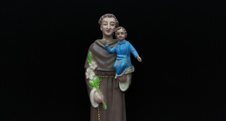 St Anthony of Padua Portuguese catholic priest sculpture or statue holding jesus christ child and white lily flower isolated on black background with copy space. Beautiful close up macro side view. - Powered by Adobe