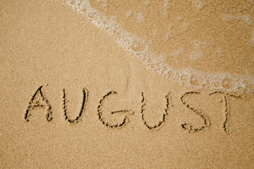 August - handwritten on the soft beach sand.