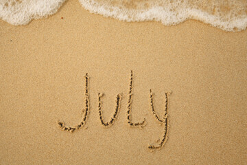 July - handwritten on the soft beach sand.