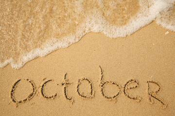 October - handwritten on the soft beach sand.